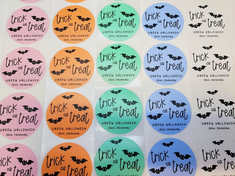 May include: A sheet of round stickers with a Halloween theme. The stickers are in various colors, including pink, orange, green, and blue. Each sticker features a black bat and the text "trick or treat" with the words "Happy Halloween" and "from, [name]" below.