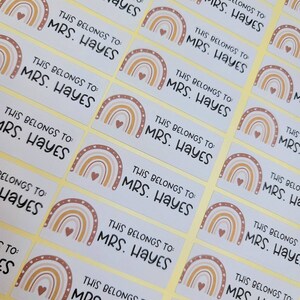 May include: A set of 12 rectangular stickers with a rainbow design and the text "This belongs to: MRS. HAYES". The stickers are on a yellow background.