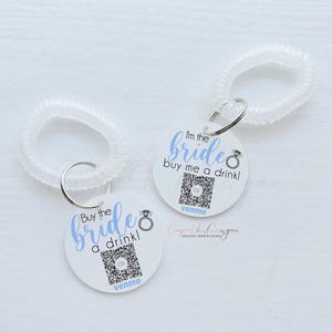 May include: Two white circular tags with black text and a blue ring design. The text on the tags reads "Buy the bride a drink!" and "I'm the bride buy me a drink!" with the Venmo logo at the bottom of each tag.
