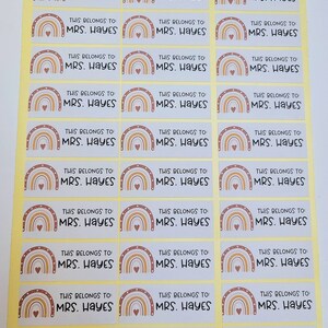 May include: A sheet of 18 personalized name labels with a rainbow design. Each label features a rainbow with a heart in the center and the text "THIS BELONGS TO MRS. HAYES".