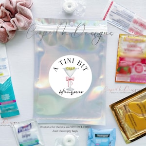May include: A clear iridescent plastic bag with a white circle sticker that says "A Tini Bit Hangover". The sticker has a pink ribbon and a martini glass with olives. The bag is filled with various items, including a pink hair scrunchie, a small white round object, a blue and white package, a yellow package with gold eye patches, and a small blue and white package.