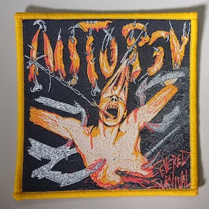 Può includere: Un cerotto ricamato nero e giallo con la parola "AUTOPSY" in un font stilizzato. Il cerotto presenta una grafica di una persona con la testa che viene tirata a pezzi da ganci di metallo. Il testo "FEVERED SURVIVAL" è in fondo al cerotto.