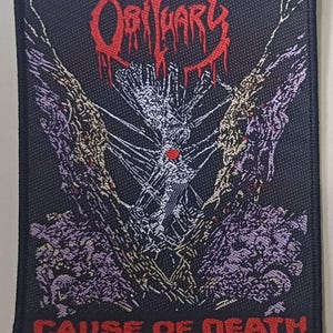 May include: Black rectangular patch featuring the band name "Obituary" in red, stylized lettering. The patch has a central skeletal design with a heart and the text "CAUSE OF DEATH" in red at the bottom. The design includes purple and yellow accents.