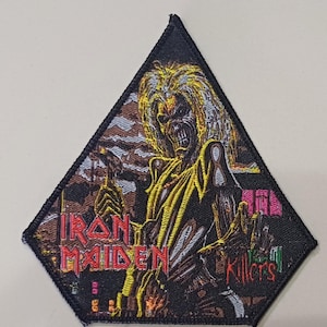 Puede incluir: Parche negro en forma de diamante con el logo de Iron Maiden y la palabra "Killers". El parche representa una figura esquelética con pelo largo y brazos extendidos, en hilo amarillo, marrón y rojo. Un artículo de temática musical.