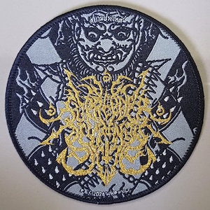 May include: A black and silver embroidered patch with a gold design. The design features a demon face with a crown and the words "WIKKULT" and "F.S.C. 2024" in a stylized font.