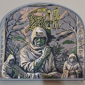 Może przedstawiać: Haftowana naszywka przedstawiająca postać w kapturze z zieloną twarzą, na tle drzew i małego budynku. Słowo "DEATH" jest wyświetlane złotymi literami nad postacią. Naszywka ma jasnoniebieską obwódkę.