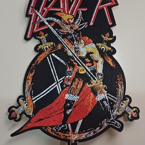 May include: Embroidered patch with the word "SLAYER" in red and white above a detailed illustration. The illustration shows a horned figure with a sword, surrounded by a pentagram and swords. The patch is mainly black, red, and gold.