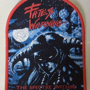 May include: A black and blue embroidered patch with red stitching. The patch features a silver glitter design of a creature with horns and the text "Fates Warning The Spectre Within".