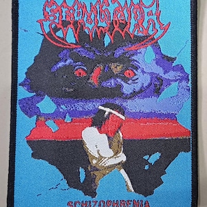 Peut inclure: Écusson brodé avec un fond bleu et une bordure noire. L'écusson présente un motif graphique avec le mot "SCHIZOPHRENIA" en bas. Le motif comprend un visage de monstre, une personne et le mot "SPORE" en rouge.