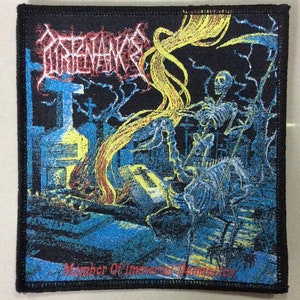 Puede incluir: Un parche tejido negro con un logotipo de banda que dice "Obituary" en letras blancas. El logotipo de la banda está sobre un gráfico de una figura esquelética que sostiene una guadaña en un escenario de cementerio. El texto "Member Of Immortal Darkness" está en la parte inferior del parche.