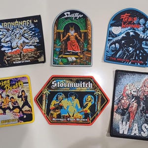 May include: A selection of six embroidered patches, each displaying a different heavy metal band logo and artwork. Bands featured include Iron Angel, Savatage, Fates Warning, Living Death, Stormwitch, and W.A.S.P. The patches are colourful and detailed.