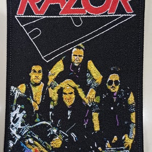 May include: Black and white embroidered patch with the word "RAZOR" in red letters. The patch features a razor blade and a band of four people.