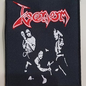 Peut inclure: Patch brodé noir avec le mot "Venom" en lettres rouges et blanches. Le patch présente une silhouette blanche de trois musiciens jouant des instruments.