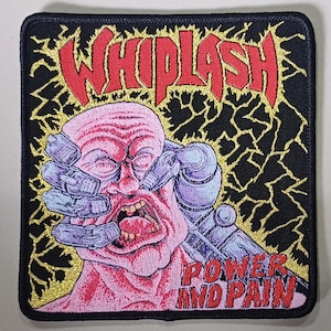 Könnte beinhalten: Gestickter Aufnäher mit dem Wort "WHIPLASH" in Rot, über einem schreienden Gesicht. Das Gesicht ist rosa mit einem Roboterarm. Die Worte "POWER AND PAIN" stehen unter dem Gesicht in Rot. Der Hintergrund ist schwarz mit goldenen Blitzen.