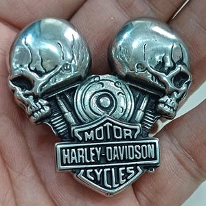 Könnte beinhalten: Silberner Motorradclub-Patch mit zwei Totenkopfköpfen und den Worten "Motor Harley-Davidson Cycles".