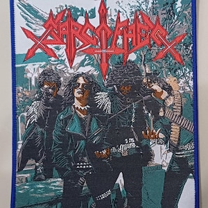 Pode incluir: Um emblema bordado retangular com borda azul apresentando uma ilustração gráfica de uma banda com cabelos longos e roupas escuras. O texto vermelho no topo diz Sarcofago. As figuras estão representadas em um ambiente florestal com tons verdes e brancos.