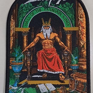 May include: Embroidered patch featuring a king seated on a throne, with the text "Hall of the Mountain King" and the band name "Savatage". The design includes pillars, lightning, and a treasure chest, with a black border.