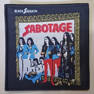 Op de afbeelding: Black Sabbath "Sabotage" patch. De patch toont de albumhoes met de bandnaam bovenaan. De artwork toont een groep mensen in verschillende outfits, met het woord "Sabotage" in het rood.