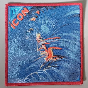 Può includere: Una toppa ricamata blu e rossa con la parola "ICON" in lettere bianche. La toppa presenta un'immagine stilizzata di un viso con uno sfondo blu e rosso.