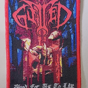 Può includere: Una toppa ricamata rossa, nera e blu con il nome della band "Opeth" in un font gotico. La toppa presenta uno scheletro con una mano insanguinata e il testo "Blood for the Blood God" in un font argentato.