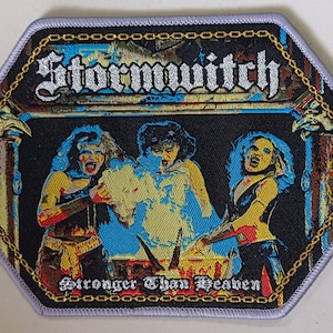 May include: A black and white embroidered patch with a gold chain border. The patch features a band called "Stormwitch" and the text "Stronger Than Heaven".