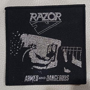 Puede incluir: Parche cuadrado negro con la palabra "RAZOR" encima de una ilustración plateada de una persona operando una máquina, con las palabras "ARMED AND DANGEROUS" debajo. El parche tiene una combinación de colores plateado y negro.