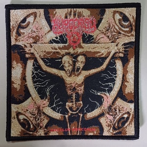 May include: A black and brown embroidered patch with a skeletal figure with two heads on a cross. The figure is surrounded by a swirling pattern of eyes and the text "OCCULUM OBSCENUM" is at the bottom.