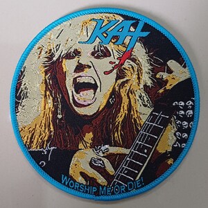 Puede incluir: Parche redondo con una cara gritando, pelo largo rubio y una guitarra. El parche tiene un borde azul y el texto "KAF" en azul. El texto "WORSHIP ME OR DIE!" está escrito en azul a lo largo del borde inferior.