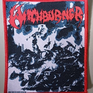 May include: A black and white embroidered patch featuring the band name "WITCHBURNER" in red lettering. The patch depicts a skull with a sword and a dark, shadowy background.