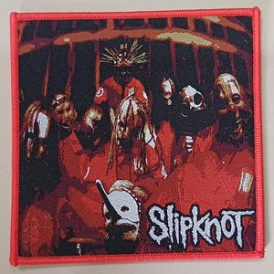 May include: A square embroidered patch with a red border featuring a graphic of the band Slipknot. The design depicts multiple figures wearing masks and red jumpsuits against a dark background, with the word Slipknot printed in white text.