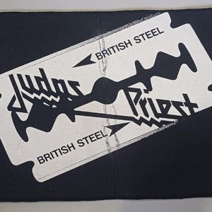 Op de afbeelding: Zwarte rechthoekige patch met een wit scheermesontwerp. De woorden "JUDAS PRIEST" en "BRITISH STEEL" staan op het mes gedrukt. Met gestikte rand.
