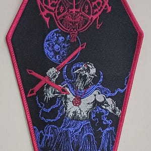 May include: Black patch with a red coffin-shaped border. The patch features a red, stylized design at the top, a blue moon, and a demonic figure holding red crossed swords. The figure is in shades of gray and blue.