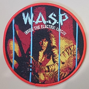 Pode incluir: Remendo bordado circular com uma borda vermelha com o nome da banda "W.A.S.P." em letras azuis claras. A imagem retrata uma pessoa com cabelo comprido e uma guitarra, com o texto "INSIDE THE ELECTRIC CIRCUS".