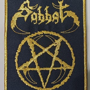 May include: Navy blue embroidered patch featuring the word "Sabbat" in gold script above a gold pentagram. The patch has a gold border.