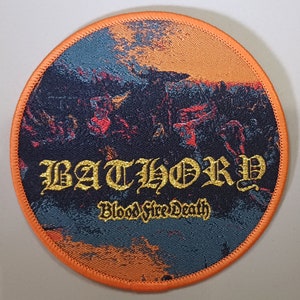 Op de afbeelding: Een ronde, oranje omrande patch met een zwart en oranje achtergrondbeeld. De bandnaam "BATHORY" is geschreven in gouden schrijfletters. De woorden "Blood Fire Death" zijn geschreven in gouden schrijfletters onder de bandnaam.