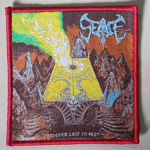 May include: Embroidered patch with a red border. It features the word "SEANCE" in blue, above a yellow and green geometric design. The patch has a detailed landscape with the text "FOREVER LAID TO REST".
