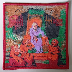 Op de afbeelding: Een rood geborduurd patch met een donkere achtergrond met een scène van vier figuren in gewaden. De figuren zijn verzameld rond een centrale figuur in een paarse gewaden. De tekst "Scream Bloody Gore" is zichtbaar in de rechterbovenhoek van de patch.