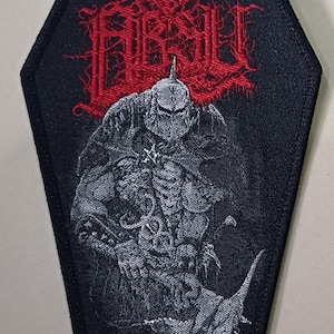 Puede incluir: Parche negro en forma de ataúd con una ilustración roja y gris. El parche presenta una imagen detallada de una figura de guerrero y la palabra "ARSUL" en rojo, con letras de estilo gótico. Texto adicional presente en la parte superior e inferior.
