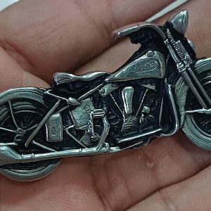 Pode incluir: Estatueta detalhada de motocicleta prateada. A motocicleta em miniatura apresenta detalhes intrincados do motor, rodas e carroceria. O design inclui um assento, guidão e farol dianteiro. O estilo geral é vintage.