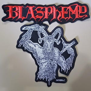 Puede incluir: Dos parches bordados. El parche superior presenta la palabra "BLASPHEME" en rojo, con letras góticas sobre un fondo negro. El parche inferior representa una ilustración blanca detallada de una figura de cabra con un pentagrama en el pecho, sobre un fondo negro.