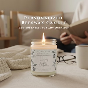 May include: A lit beeswax candle in a clear glass jar with a white label featuring botanical illustrations and the text "Rose Creek Candle Co. LLC" and "Happy Birthday". The label also includes the text "Net Wt 14 oz (397 g)".