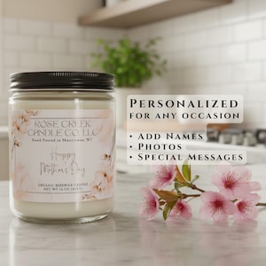 May include: A 16 oz organic beeswax candle in a clear glass jar with a black lid. The label features floral illustrations, the text Rose Creek Candle Co. LLC, Happy Mother's Day, and net weight 16 oz (454 g). A branch of pink cherry blossoms sits nearby.