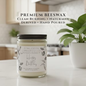 May include: A 16 oz. beeswax candle in a clear glass jar with a black lid. The label reads PREMIUM BEESWAX CLEAN BURNING NATURALLY DERIVED HAND POURED, ROSE CREEK CANDLE CO. L.L.C, Happy Birthday, and NET WT 16 OZ. (454 G) with botanical illustrations.
