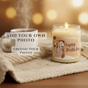 May include: A clear glass jar candle with a lit wick and a custom label featuring a photograph of a person and the text Happy Birthday, placed next to a white ceramic mug with steam rising, both resting on a textured cream-colored knit fabric.