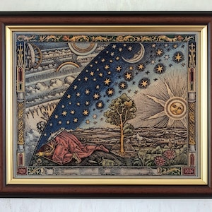 May include: A framed tapestry depicting a person in a red robe kneeling on a landscape, peering through the edge of the sky to reveal a celestial expanse of stars, a crescent moon, and a radiant sun with a face, all within a dark wood frame.