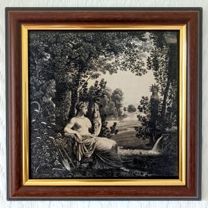 May include: A framed black and white print featuring a classical scene with a seated figure, trees, and a waterfall. The print is in a dark brown frame with a gold inner border. The artwork is a detailed illustration, creating a vintage aesthetic.