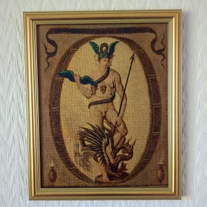 May include: A framed artwork depicting a classical figure with a winged helmet, holding a spear and a blue cloth. The figure stands on a winged creature. The artwork is set within an oval frame, surrounded by a gold frame.