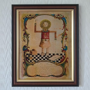 Könnte beinhalten: Ein gerahmter Druck mit einer zentralen Figur mit sonnenförmigem Kopf, die eine rote Schürze trägt und auf einem schwarz-weiß karierten Boden steht. Das Bild enthält verzierte blau-goldene Ränder, verschiedene Werkzeuge und den Text A Free Mason.