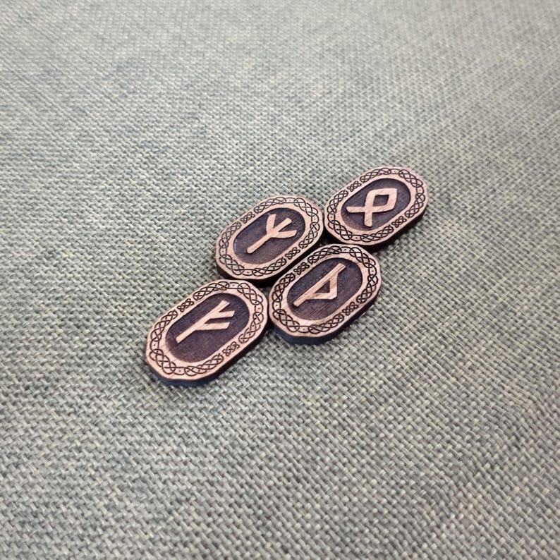 May include: Four oval-shaped, dark grey rune stones with etched symbols and decorative borders. The runes are in a light grey colour. The stones are arranged on a textured, light green surface.