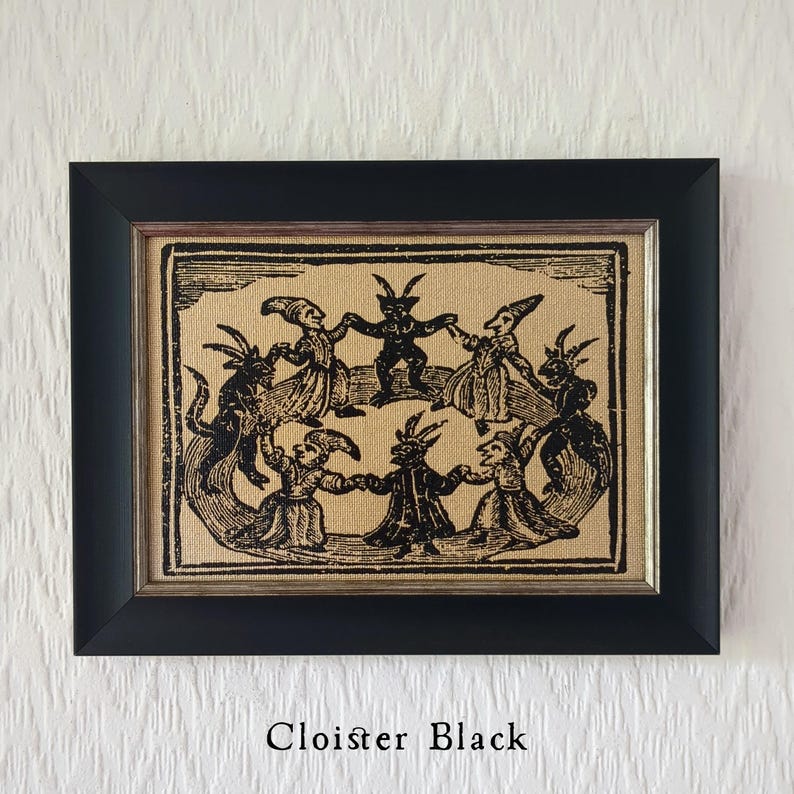 May include: Black framed artwork featuring a vintage illustration of figures with horns and cloaks dancing in a circle. The artwork is printed on a tan fabric and the text "Cloister Black" is at the bottom.
